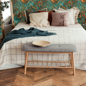 Bedroom with ornate wall pattern, wooden bench, and checkered bedspread and fun, abstract wallpaper.